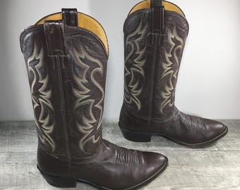 May include: A pair of brown leather cowboy boots with a pointed toe and a decorative stitch pattern. The boots have a tall shaft and a pull-on design.