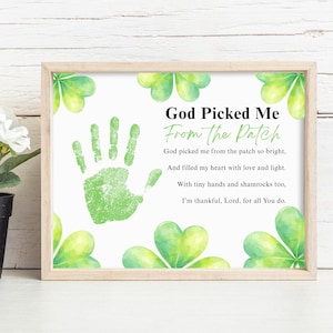 Puede incluir: Una impresión enmarcada con el texto "God Picked Me From the Patch" y una huella de mano verde. La impresión está decorada con tréboles de acuarela. El marco es de color marrón claro.