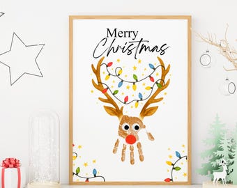 Könnte beinhalten: Ein gerahmter Weihnachtskunst-Druck mit einem Rentier-Design, das aus einem Handabdruck gefertigt wurde. Das Rentier hat braunes Geweih, eine rote Nase und ist mit bunten Weihnachtslichtern geschmückt. Die Worte "Merry Christmas" stehen über dem Rentier.