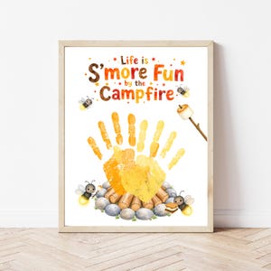 May include: A white art print featuring the text Life is S'more Fun by the Campfire in colourful letters. Below the text is a yellow handprint resembling flames over a log fire, surrounded by three illustrated fireflies and a marshmallow on a stick.