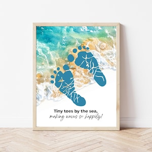 May include: A framed print featuring blue footprints on a beach scene. The artwork includes the text "Tiny toes by the sea, making waves so happily!" The background shows ocean waves and a sandy shore, all within a light wooden frame.