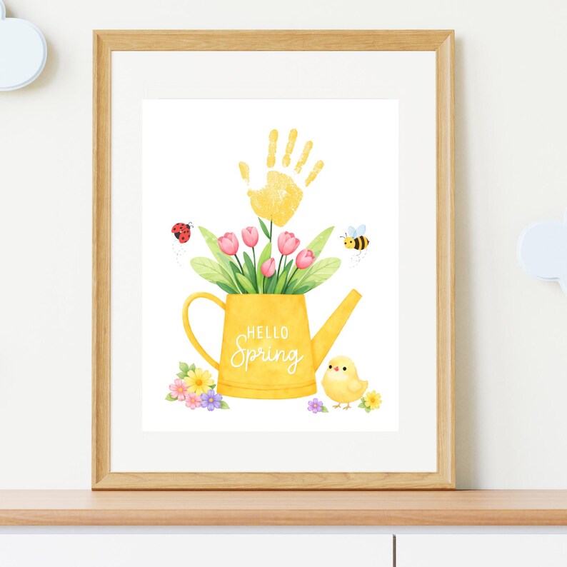 Puede incluir: Impresi&oacute;n acuarela enmarcada. Una regadera amarilla con el texto "Hello Spring" contiene tulipanes rosas, hojas verdes y una huella de mano amarilla. Tambi&eacute;n se representan una mariquita, una abeja y un pollito.