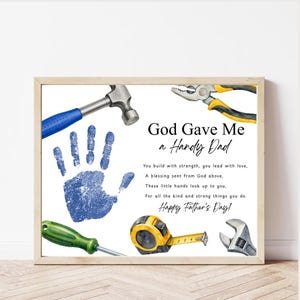 May include: A framed print with a light wood frame features a blue handprint and watercolor illustrations of tools. Text reads "God Gave Me a Handy Dad" with a Father's Day message. A hammer, pliers, and wrench are shown.