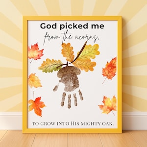May include: A framed wall art print featuring the text God picked me from the acorns, to grow into His mighty oak. The design includes a brown handprint shaped like an acorn with oak leaves and scattered orange and yellow autumn leaves.