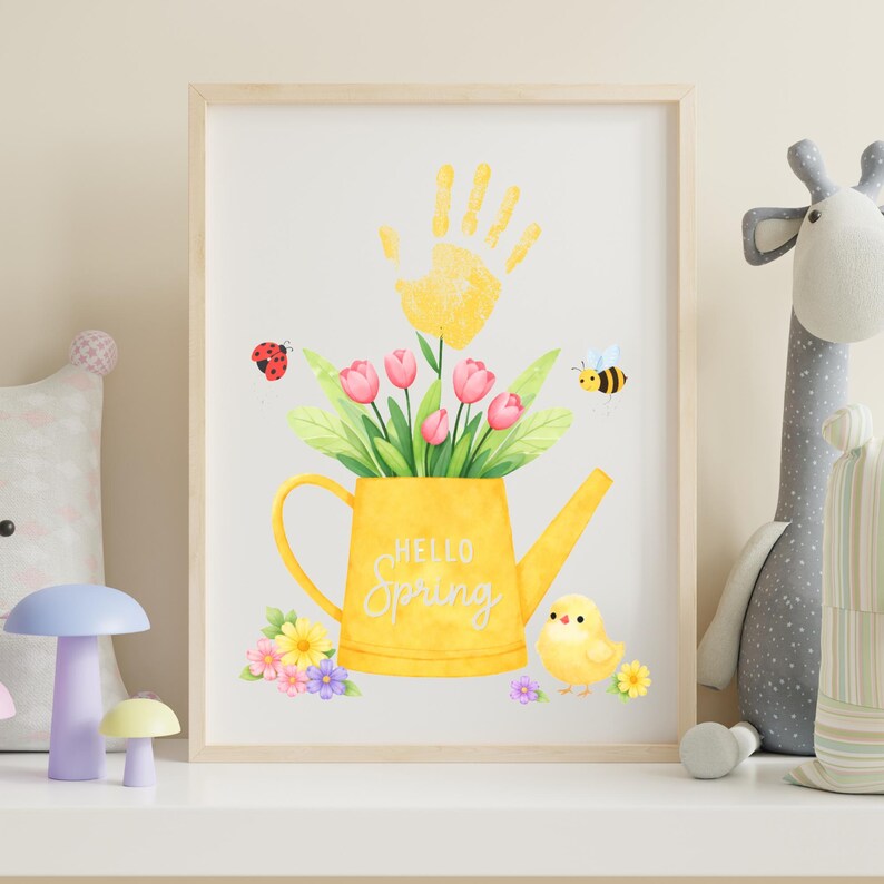 Puede incluir: Una impresi&oacute;n enmarcada con una ilustraci&oacute;n en acuarela de una regadera amarilla llena de tulipanes rosas y hojas verdes. Una huella de mano amarilla est&aacute; encima de la regadera. Las palabras "Hello Spring" est&aacute;n en la regadera. Una mariquita, una abeja y un pollito tambi&eacute;n est&aacute;n en la imagen.