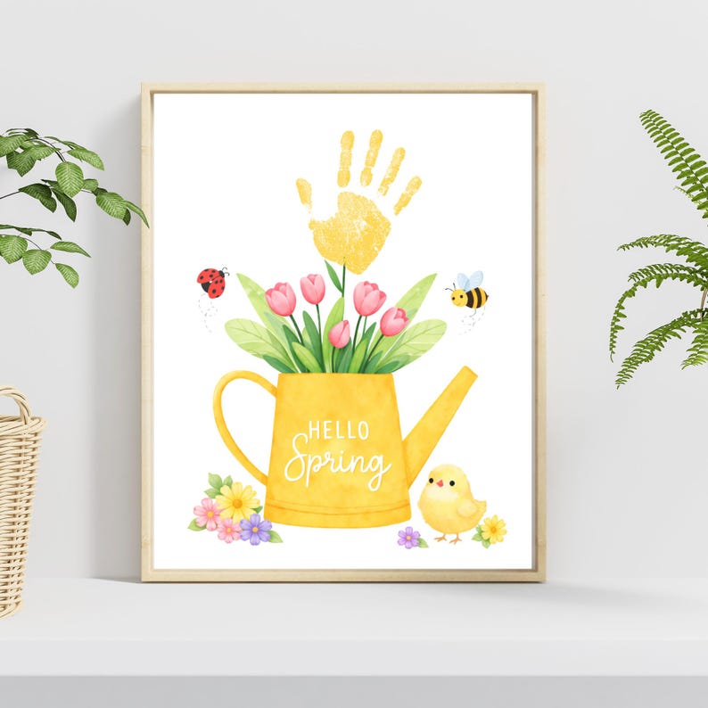 Puede incluir: Una impresi&oacute;n enmarcada con acuarela que presenta una regadera amarilla llena de tulipanes rosas y hojas verdes. Una huella de mano amarilla est&aacute; encima de la regadera. Las palabras "Hello Spring" est&aacute;n escritas en la regadera. Tambi&eacute;n se muestra una mariquita, una abeja y un pollito.