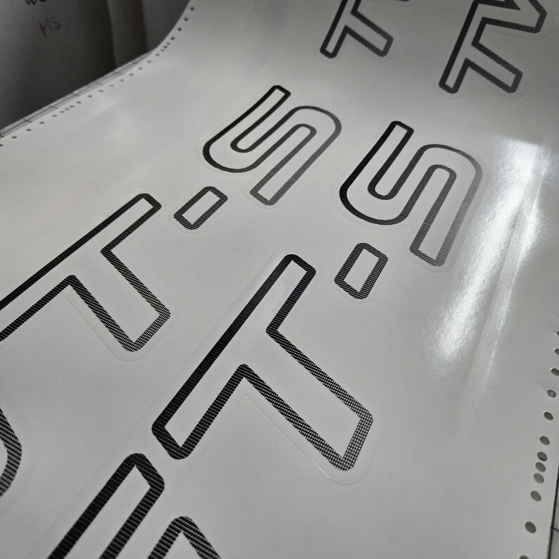 May include: A sheet of white stickers featuring the word "SOFT" repeated in a bold, sans-serif font. The letters are outlined in black with a textured fill. The sheet has perforated edges for easy separation.