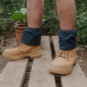 May include: A pair of tan work boots with black laces and blue gaiters. The boots are on a wooden platform.