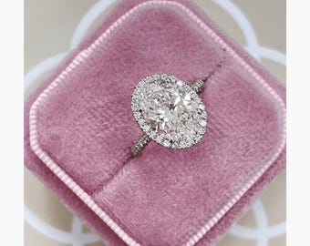May include: A silver-toned ring featuring a large, oval-cut center stone surrounded by a halo of small, round, brilliant-cut stones. The band is thin and also encrusted with small, round, brilliant-cut stones along the visible upper portion.