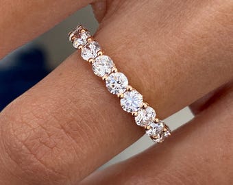 May include: Rose gold band ring featuring a continuous row of round, brilliant-cut diamonds. The diamonds are set closely together, creating a sparkling, elegant look. The ring is shown on a finger, highlighting its design and craftsmanship.