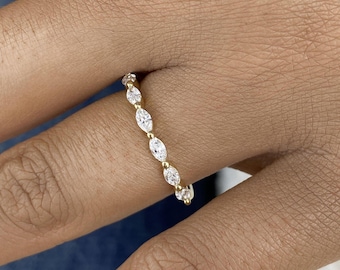 May include: A gold band ring featuring a series of clear, marquise-cut stones set in a row. The stones are arranged vertically along the finger, held in place by small gold prongs between each individual marquise-shaped gemstone.