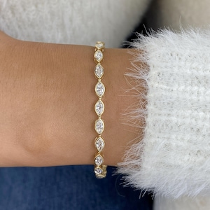 Puede incluir: Un brazalete de oro con piedras preciosas de talla marquesa. El brazalete está engastado en una banda de oro y se lleva en la muñeca. Las piedras preciosas son claras y brillantes, creando una joya delicada y elegante.