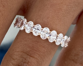 May include: A rose gold eternity ring with a continuous line of oval-cut diamonds. The diamonds are set closely together, creating a sparkling band. The ring is displayed on a finger, showcasing its elegant design.