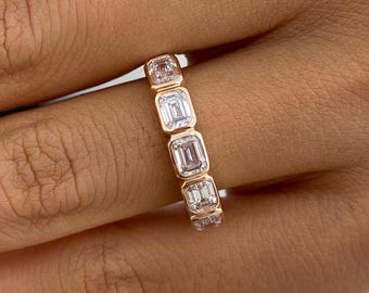 May include: A rose gold band featuring a series of five rectangular emerald-cut clear stones set in a bezel style. The stones are arranged vertically along the band, showcasing a clean, metallic frame around each individual gemstone.
