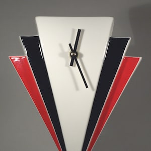 May include: A white ceramic clock with black hands and a gold centre. The clock face is surrounded by red and black geometric shapes.
