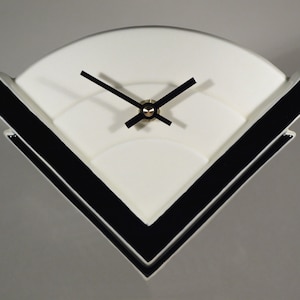 May include: A white ceramic clock with black accents in the shape of a triangle. The clock face is white with black hands.