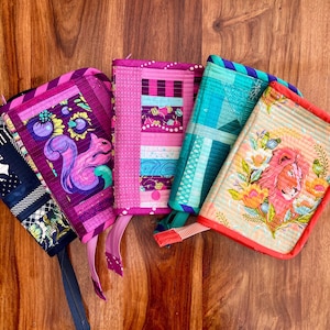 May include: A collection of colorful, quilted fabric pouches with various designs. One features a squirrel, another a lion, and others have geometric patterns. Each pouch has a zipper or ribbon closure.