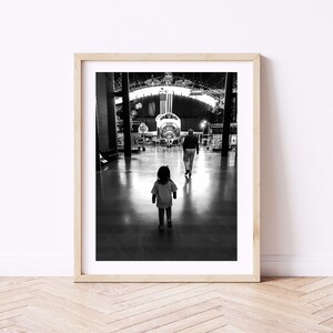 May include: A black and white photograph of a child and an adult walking towards a large aircraft in a hangar.