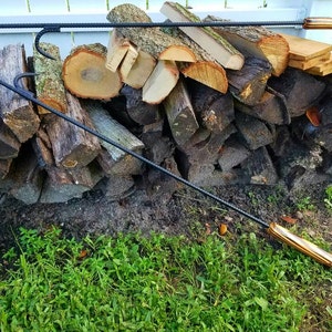 May include: Two black metal fireplace tools with wooden handles. The tools are lying on a pile of stacked firewood.