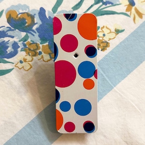 May include: A white rectangular block with a polka dot pattern in pink, blue, orange, and black.