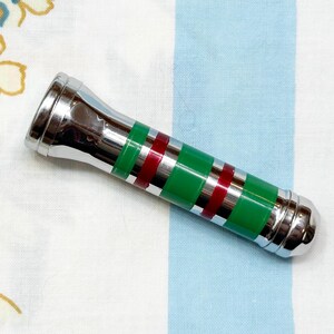 May include: A chrome bottle stopper with green and red bands. The stopper has a cylindrical shape with a flared top and a rounded bottom. The bands are evenly spaced around the body of the stopper.