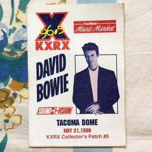 May include: A vintage KXRX David Bowie collector's patch. The patch features the text "DAVID BOWIE" in bold, blue letters, and an image of David Bowie. The patch also includes the text "TACOMA DOME MAY 21, 1990".