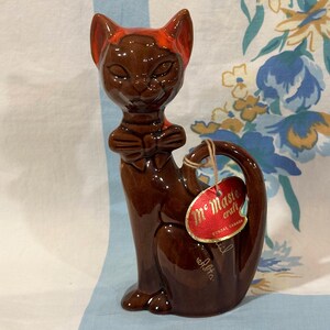 May include: A brown ceramic cat figurine with a red bow tie and ear accents. The cat has a curved tail and a tag that reads "Mr. Master Craft, Dundas Canada."