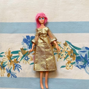May include: A vintage doll with pink hair and blue eyes wearing a gold dress with a mesh overlay.