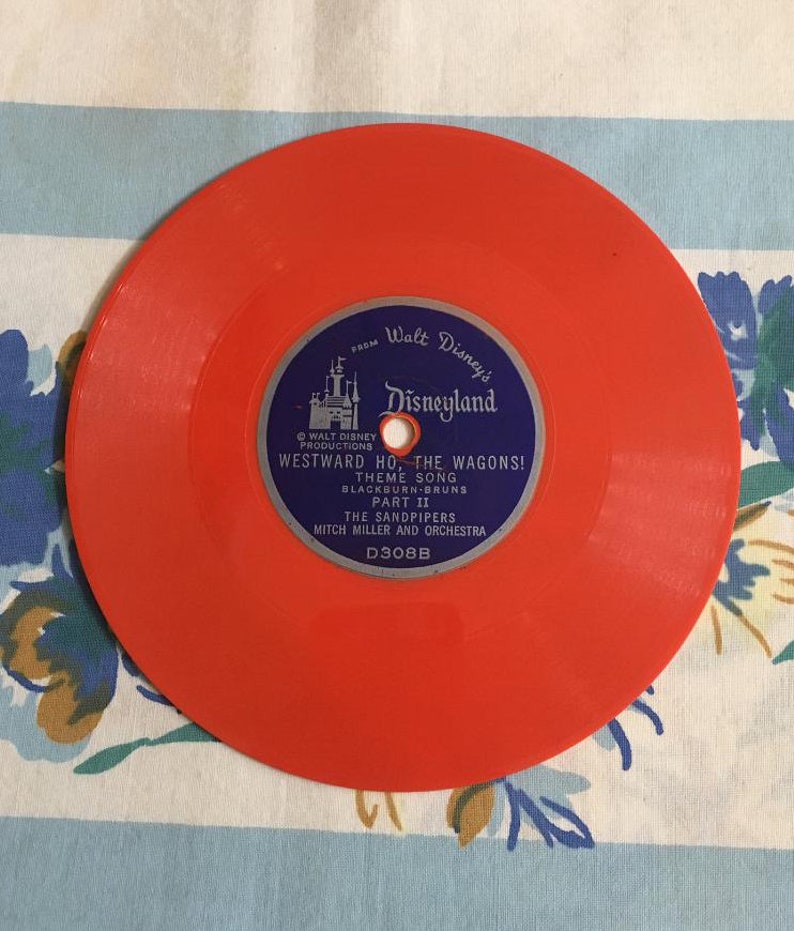 May include: A bright orange vinyl record with a blue label featuring Walt Disney's Disneyland logo and the text "Westward Ho, The Wagons! Theme Song, Part II, The Sandpipers, Mitch Miller and Orchestra, D308B".