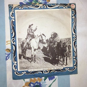 May include: A vintage record sleeve featuring a black and white photo of a cowboy riding a horse. The text on the sleeve reads "from Walt Disney's Westward Ho, The Wagons!" and "25c".