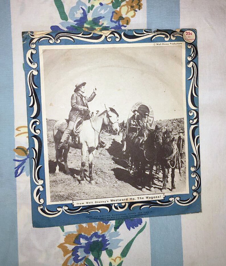 May include: A vintage record sleeve featuring a black and white photo of a cowboy riding a horse. The text on the sleeve reads "from Walt Disney's Westward Ho, The Wagons!" and "25c".