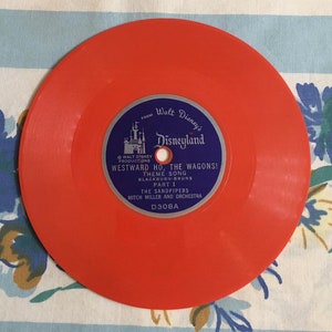May include: Orange vinyl record with a blue label featuring Walt Disney's Disneyland logo and the text "Westward Ho, The Wagons! Theme Song, Blackburn-Bruns, Part I, The Sandpipers, Mitch Miller and Orchestra, D308A."