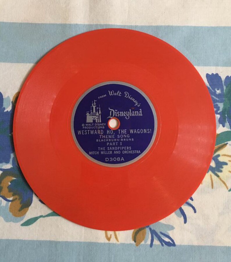 May include: Orange vinyl record with a blue label featuring Walt Disney's Disneyland logo and the text "Westward Ho, The Wagons! Theme Song, Blackburn-Bruns, Part I, The Sandpipers, Mitch Miller and Orchestra, D308A."