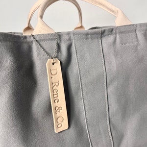 May include: A gray canvas tote bag with cream colored handles and a leather tag that says "D. Rene & Co."