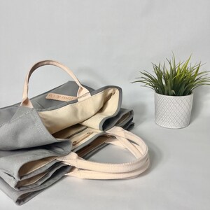 May include: A gray canvas tote bag with a cream colored lining and a leather tag that says "Keno & Co."