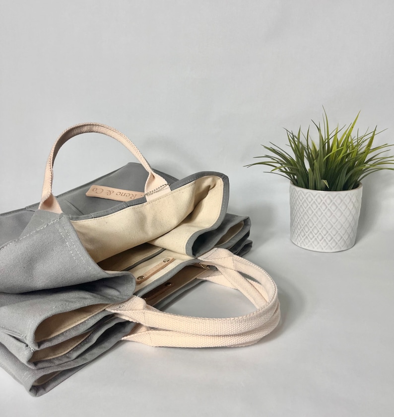 May include: A gray canvas tote bag with a cream colored lining and a leather tag that says "Keno & Co."