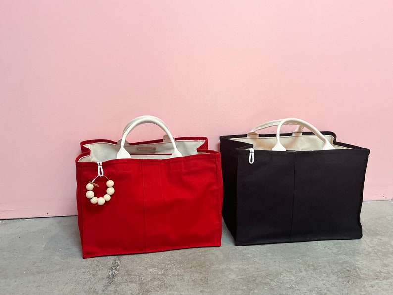 May include: Two tote bags, one red and one black, with white handles. The red bag has a wooden bead charm attached to it.