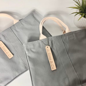 May include: Two gray canvas tote bags with cream colored handles and leather tags that say "D. Rene & Co."