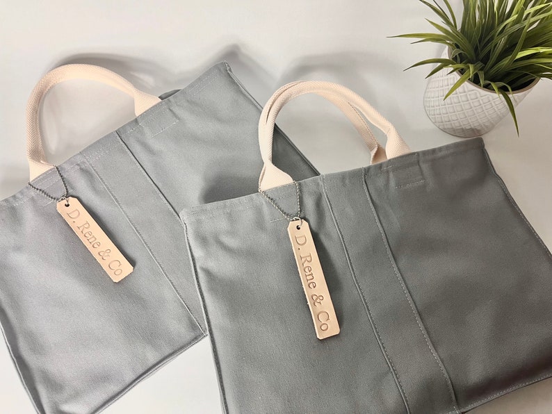 May include: Two gray canvas tote bags with cream colored handles and leather tags that say "D. Rene & Co."