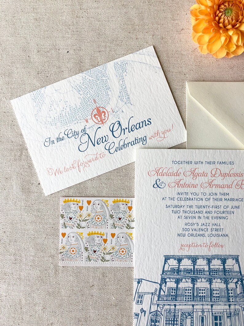 May include: Wedding invitation with a blue and white illustration of a building in New Orleans, Louisiana. The text reads "In the City of New Orleans We look forward to Celebrating with you!" and "Adelaide Agata Duplessis & Antoine Armand F. Invite you to join them at the celebration of their marriage Saturday the twenty-first of June two thousand and fourteen at seven in the evening Rosy's Jazz Hall 500 Valence Street New Orleans, Louisiana reception to follow."