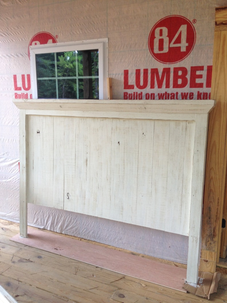 May include: White painted headboard with a simple design. The headboard is made of wood planks and has a slightly distressed look. The headboard is sitting on a wooden floor.
