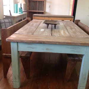 May include: A rustic farmhouse style dining table with a distressed light blue finish. The table has a wooden top and is surrounded by two matching benches.