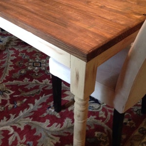 May include: A wooden dining table with a dark brown tabletop and cream-colored legs. The table is paired with upholstered chairs. The table's dimensions are not visible in the image.
