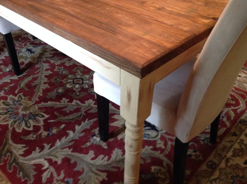 May include: A wooden dining table with a dark brown tabletop and cream-colored legs. The table is paired with upholstered chairs. The table's dimensions are not visible in the image.