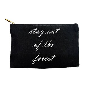 Könnte beinhalten: Schwarze rechteckige Reißverschlusstasche mit dem Text "stay out of the forest" in weißer Schrift. Die Tasche hat einen goldfarbenen Reißverschluss und einen weißen Hintergrund.