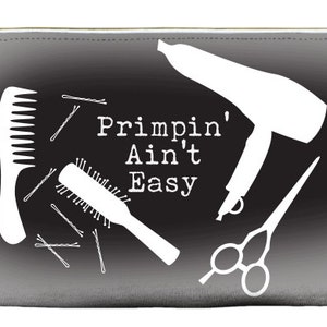 May include: Black and white makeup bag with a zipper closure. The bag features a hair dryer, comb, brush, scissors, and bobby pins. The text "Primpin' Ain't Easy" is printed on the bag.