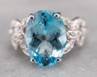 May include: A silver ring with a large oval-shaped blue topaz gemstone set in a delicate, intricate design.