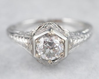 May include: A vintage engagement ring with a hexagonal setting and a round brilliant cut diamond. The band is decorated with intricate filigree details.