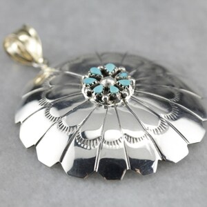 Könnte beinhalten: Ein silberner Anhänger mit einem türkisfarbenen Stein in der Mitte und einem Blumendesign. Der Anhänger ist aus Sterlingsilber gefertigt und hat ein detailliertes Design.
