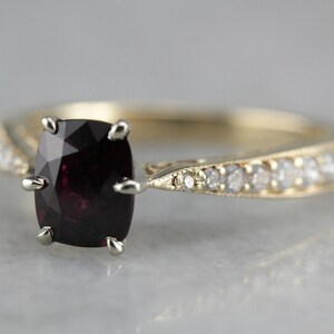 May include: A gold ring featuring a dark red gemstone and a row of small diamonds on the band.